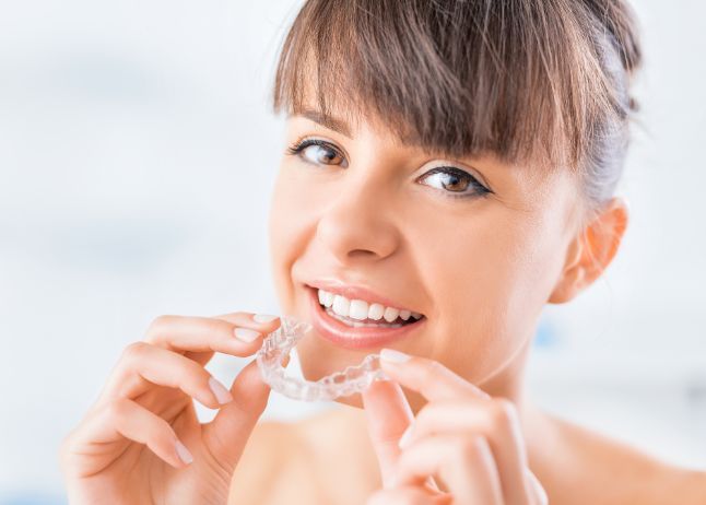 Woman holding clear aligner, smiling, preparing to put it in her mouth.
