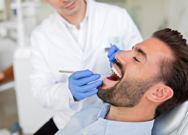 Dentist examining a man's teeth in a dental office. Man's mouth is open, dentist wears gloves and white coat.