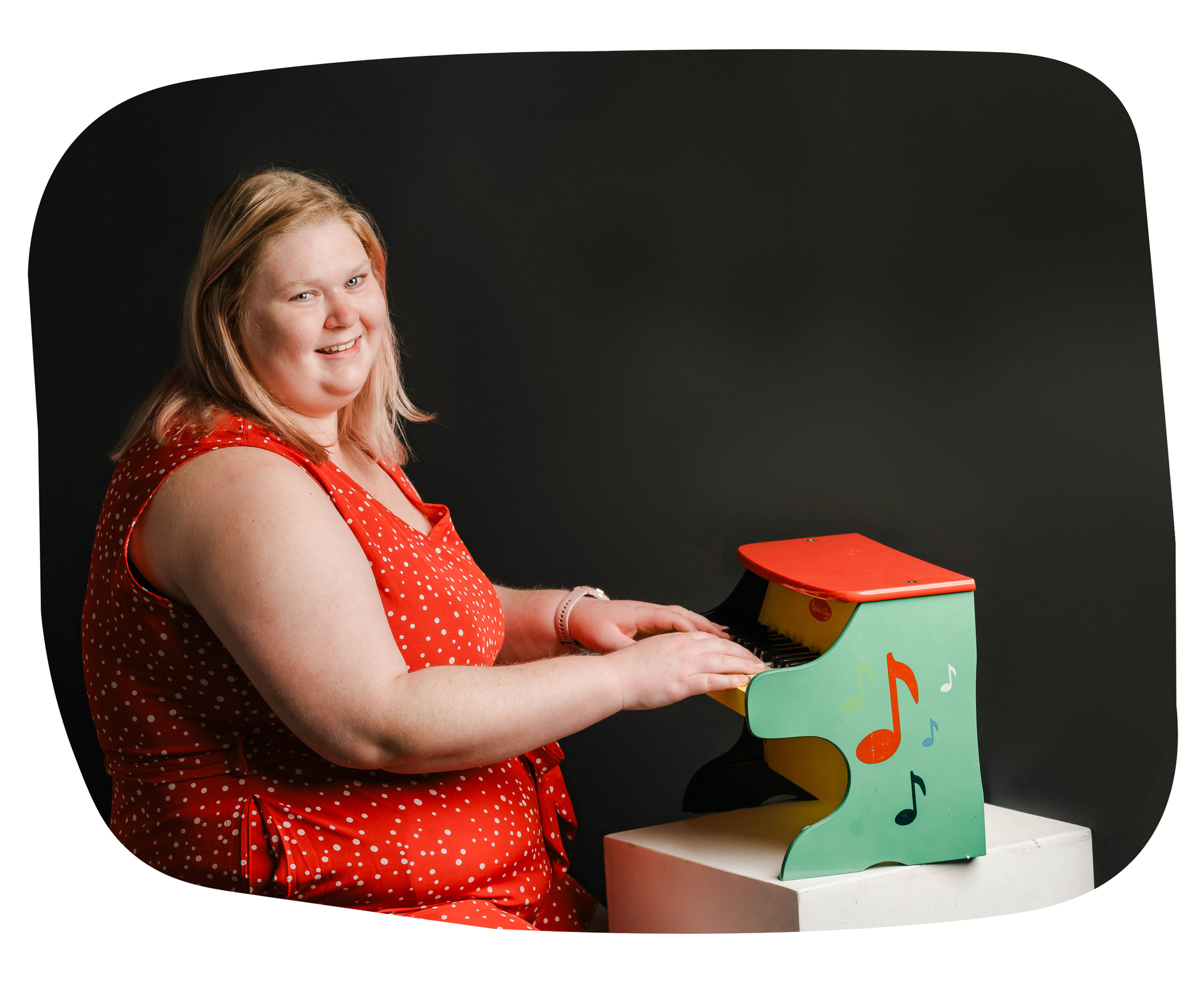 A woman in a red dress is playing a small toy piano.