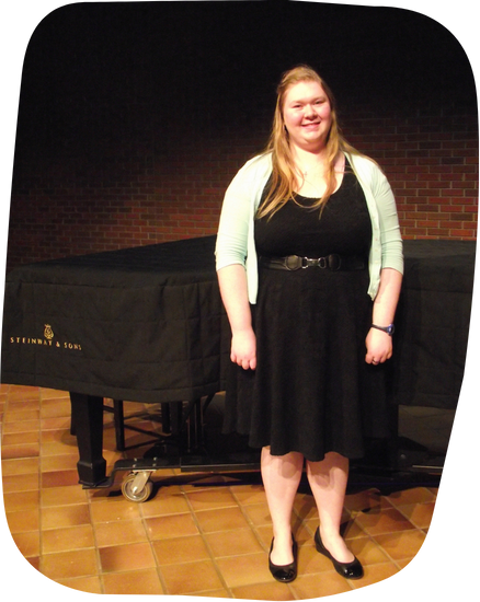 A woman in a black dress stands in front of a steinway piano