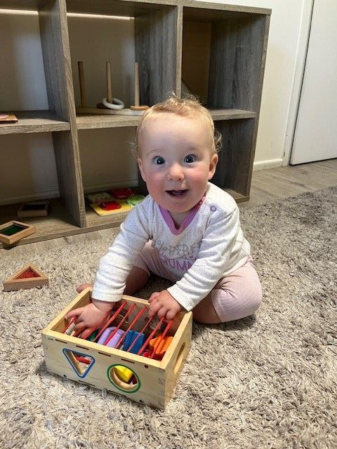 A Baby Is Sitting On The Floor Playing With A Wooden Toy – Bundaberg North, QLD - Cradle to Crayons Education & Care