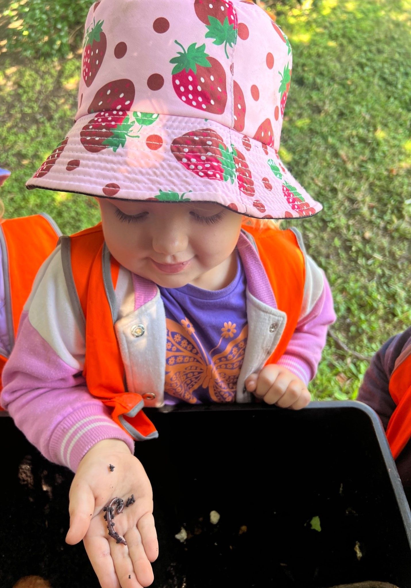 A Little Girl In A Pink Hat Is Sitting On The Grass – Bundaberg North, QLD - Cradle to Crayons Education & Care