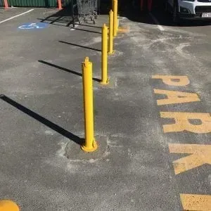 A row of bright yellow bollards stands in a parking lot, near a painted handicap symbol and partial parking text.