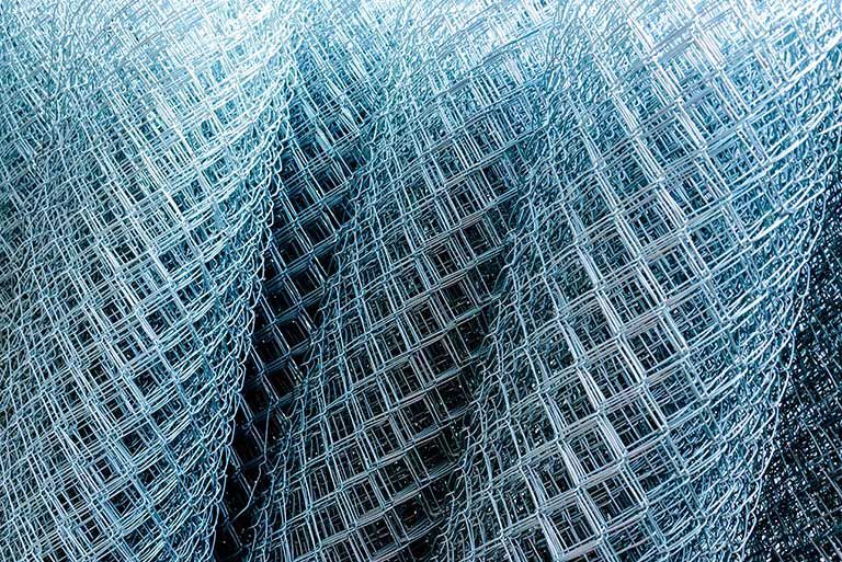 A close-up view of a metallic, silver-colored wire mesh screen with a diagonal grid pattern, folded in overlapping layers.