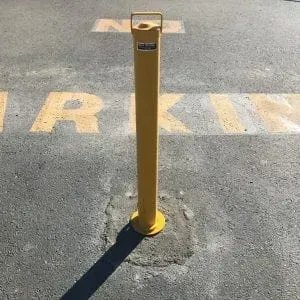 A yellow bollard installed in an asphalt parking space marked with the words 