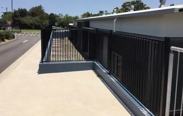 A view of a building exterior with a ramp and black metal railing beside a concrete sidewalk.