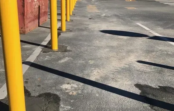A row of bright yellow bollards stands on an asphalt surface, casting long shadows across the ground.