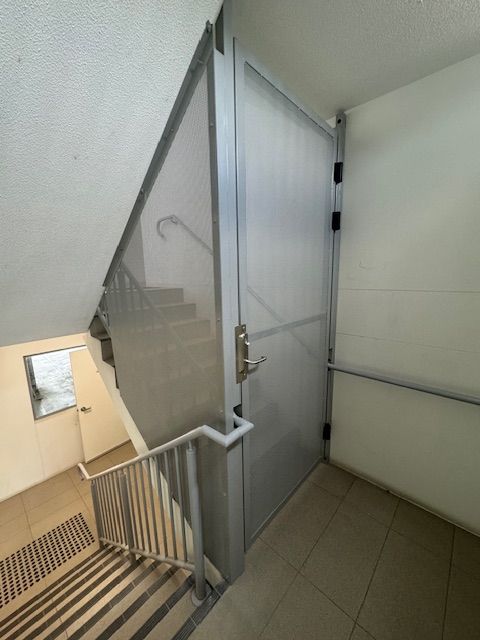 A stairwell features a beige wall, a metallic handrail, and a frosted glass door leading to a landing with light flooring.