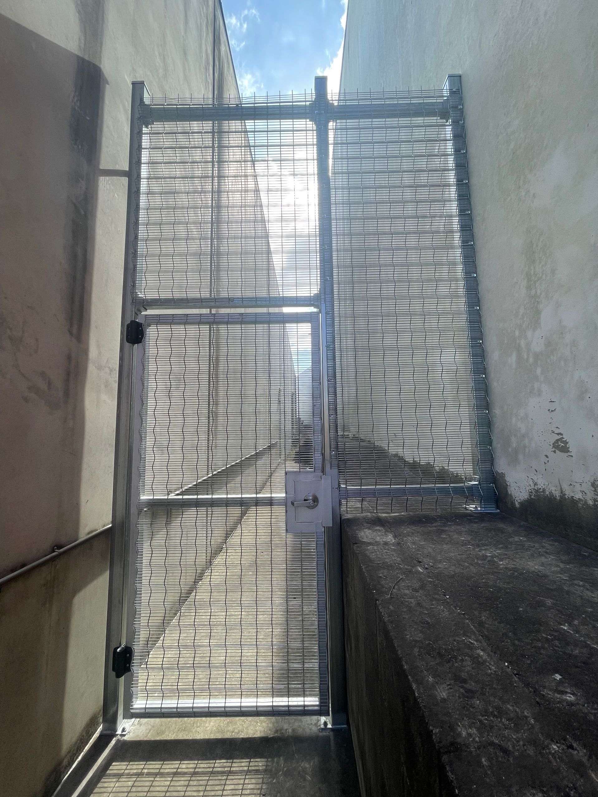 A metal security gate with sharp, outward-pointing spikes installed in a narrow alleyway between two concrete walls.