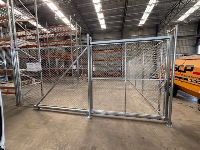 A chain-link sliding gate installed inside a large warehouse with metal storage racking.