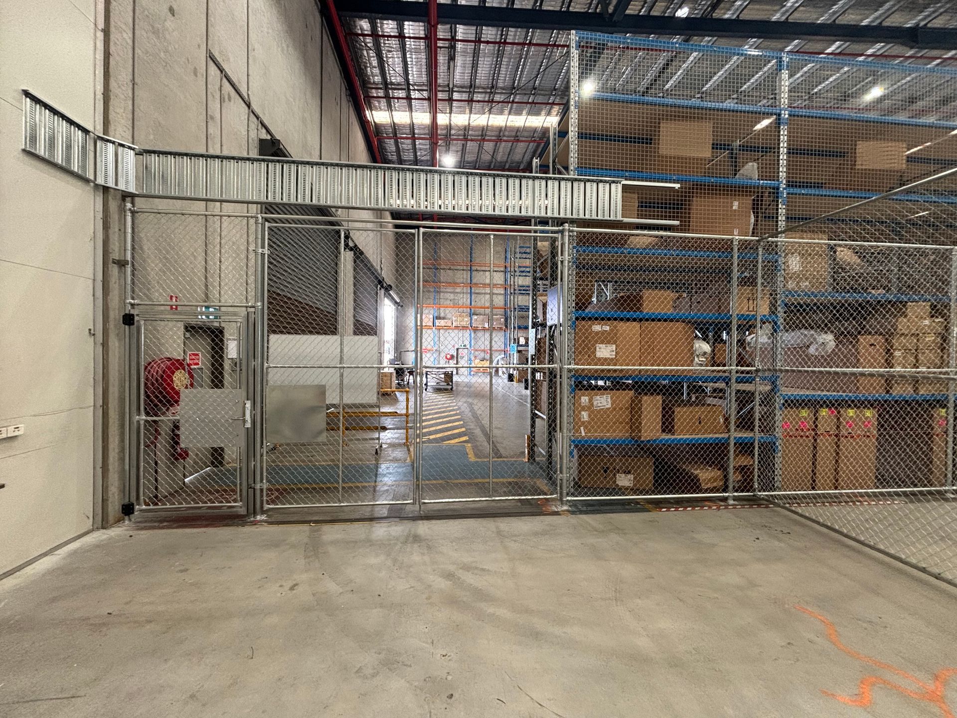 A warehouse storage area with metal fencing, a secure gate, and shelves stacked with cardboard boxes.