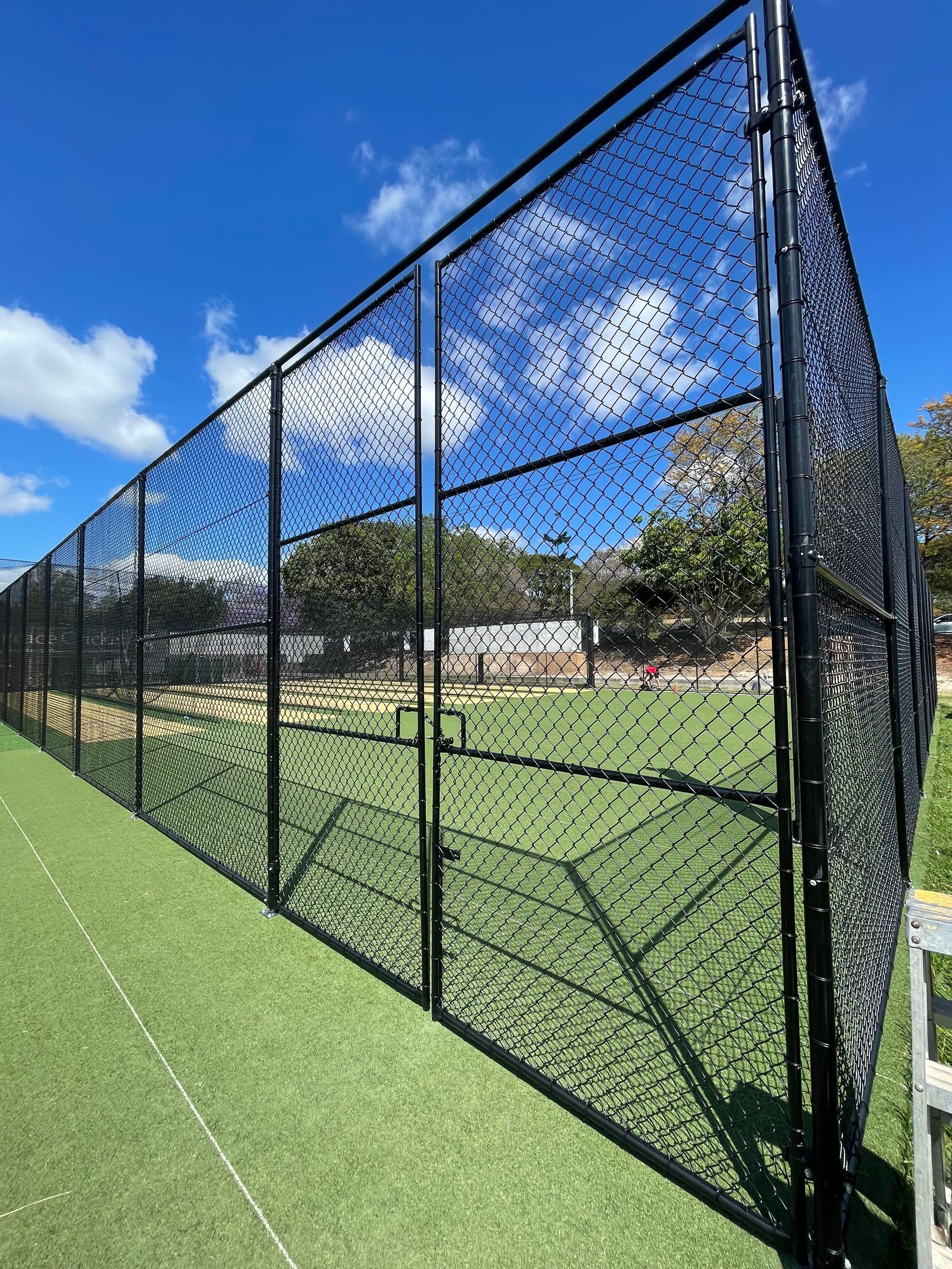 A tall black chain-link fence encloses an artificial turf sports field under a clear blue sky.