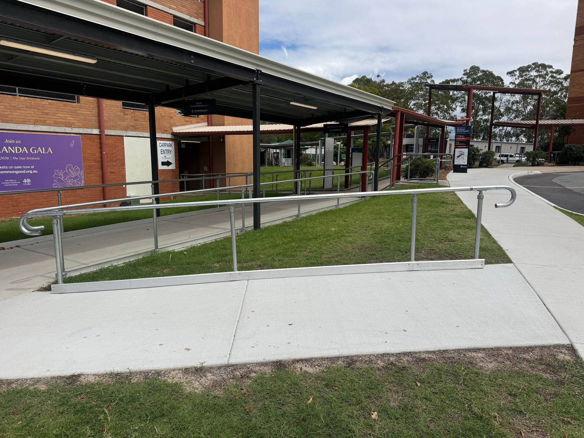 A concrete wheelchair ramp with silver metal handrails leading to a covered building entrance on a sunny day.