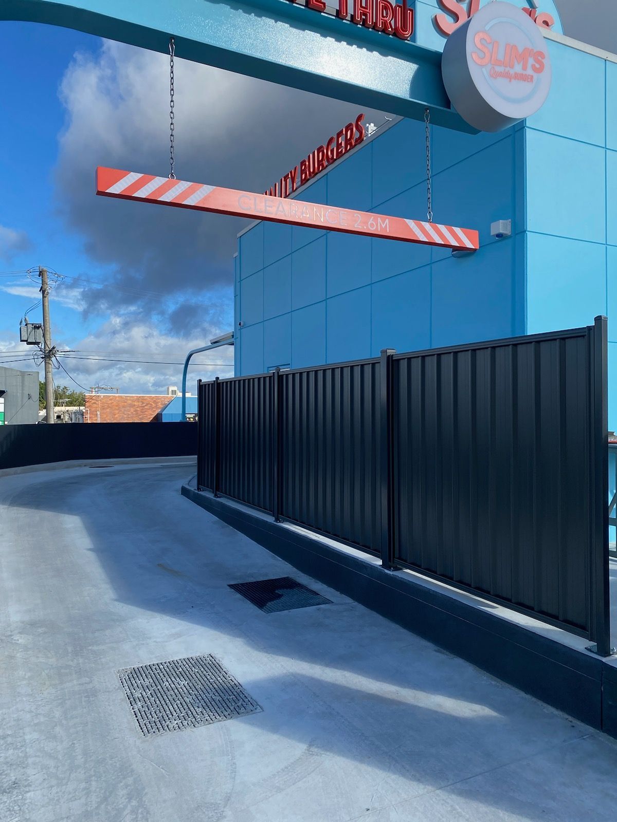 Drive-thru entrance at Slim's restaurant with a low-clearance height bar hanging from a blue overhead structure.