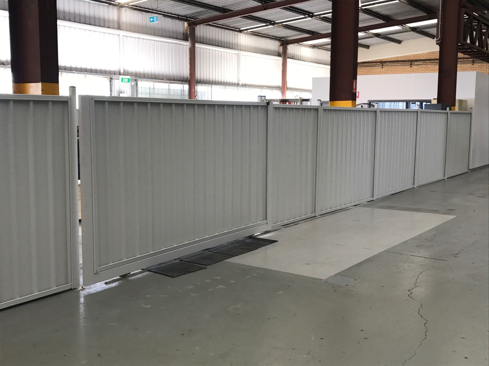 A tall, grey corrugated metal privacy fence surrounds a white industrial storage tank on a concrete base.