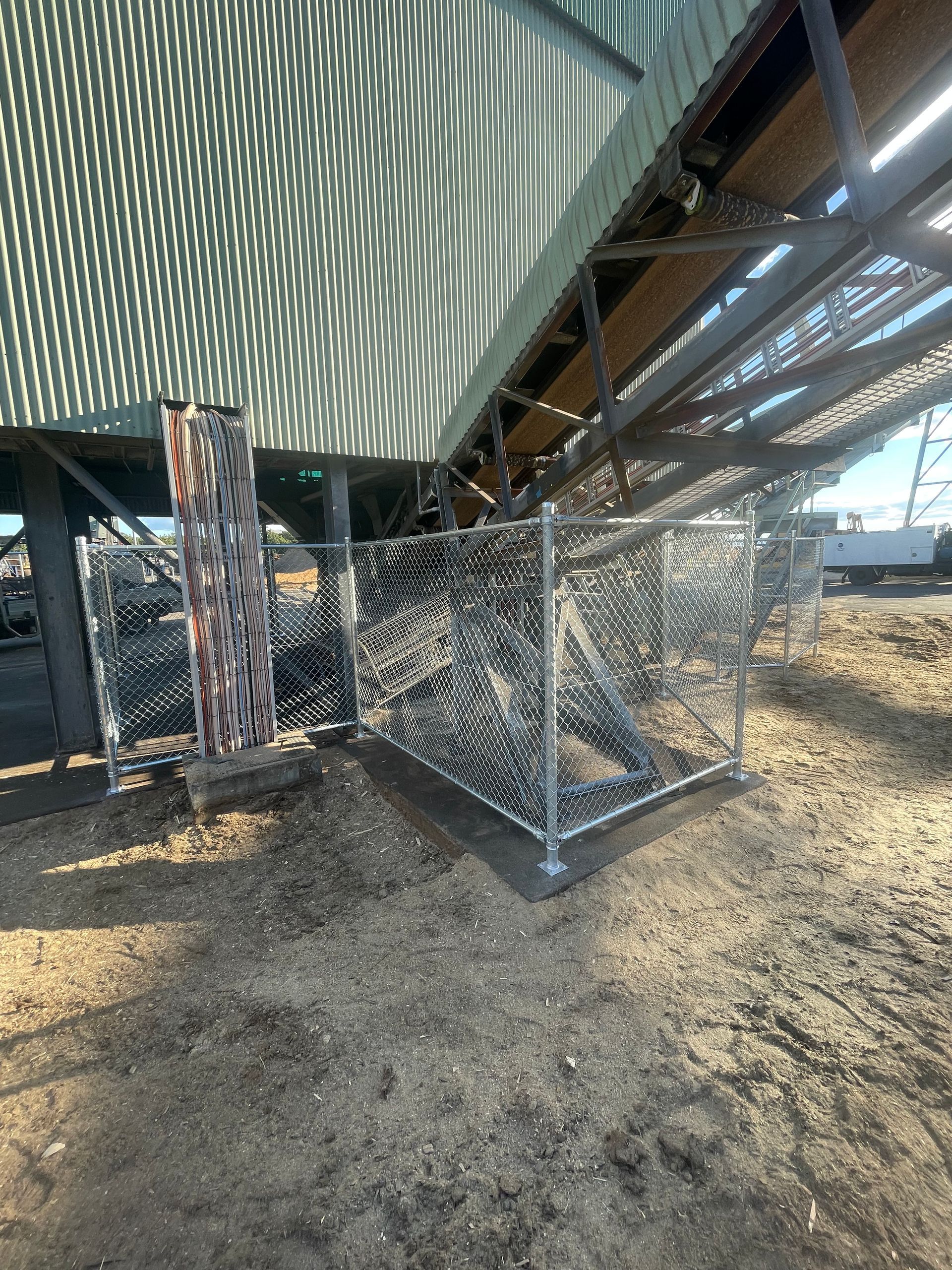 A square chain-link fence enclosure covered in camouflage netting beneath a curved, corrugated metal structure.