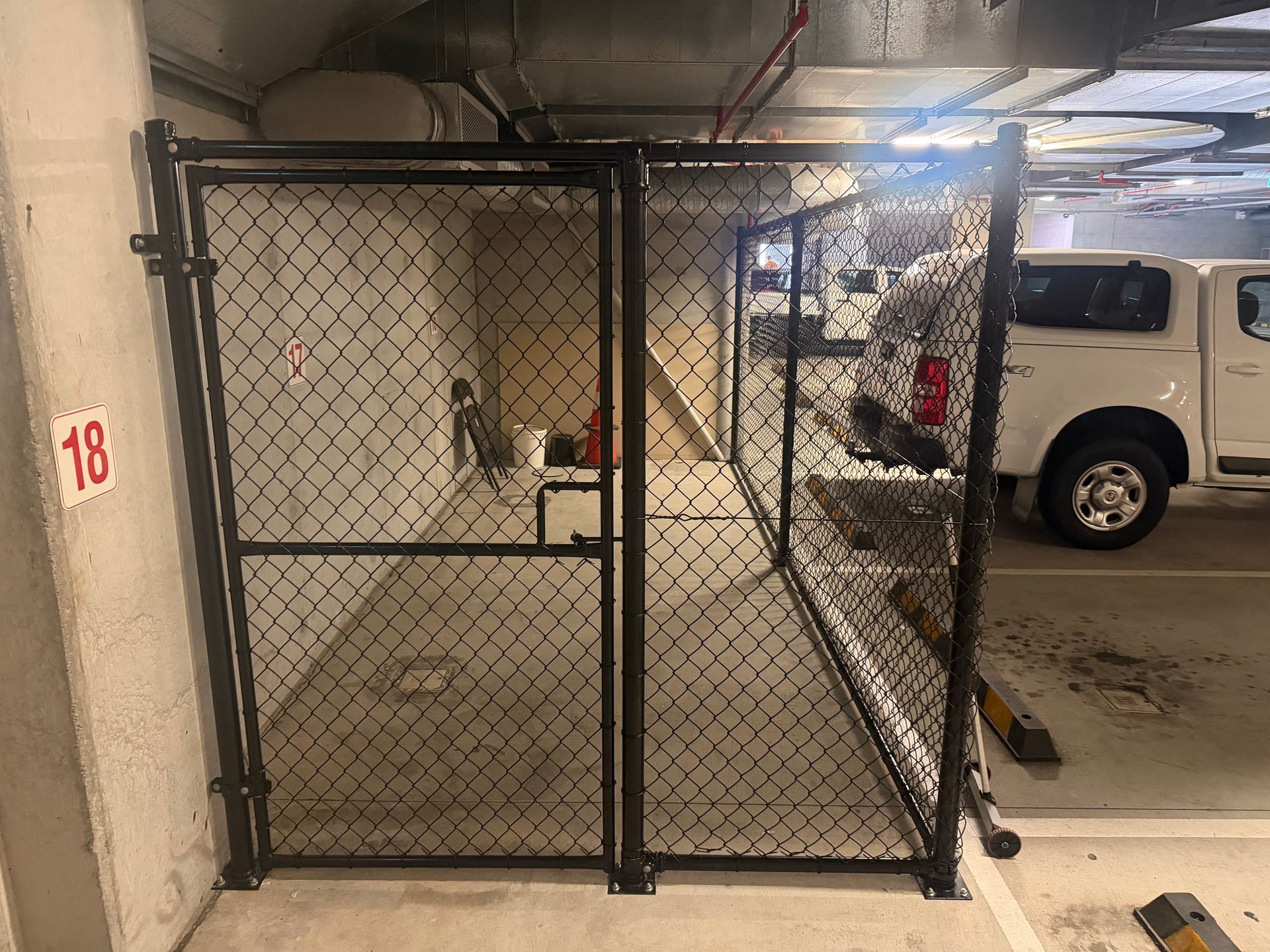A white commercial truck parked behind a large chain-link gate in front of an industrial building.