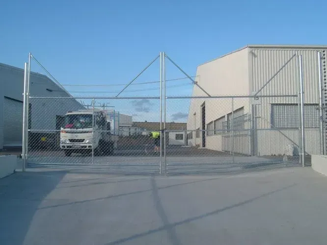 A white commercial truck parked behind a large chain-link gate in front of an industrial building.