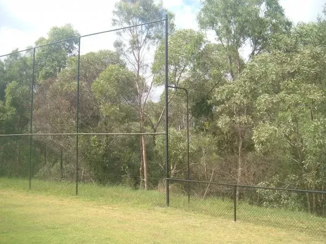 A black metal fence standing in a grassy field in front of a dense forest.