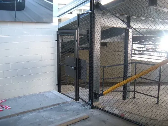 A black metal gate and chain-link fence barrier at the edge of a concrete parking structure with a yellow safety bar.