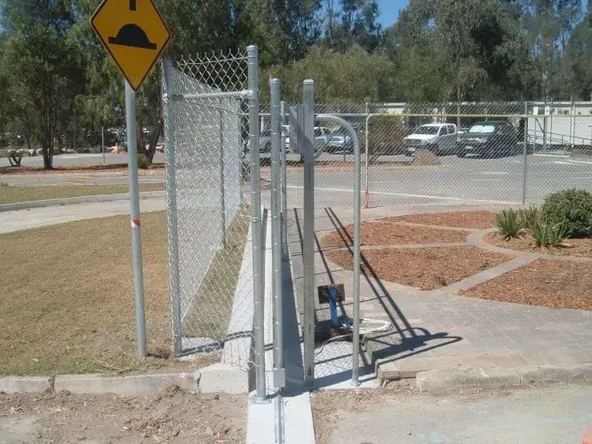 A yellow speed bump sign stands next to a metal chain-link fence bordering a paved parking lot.
