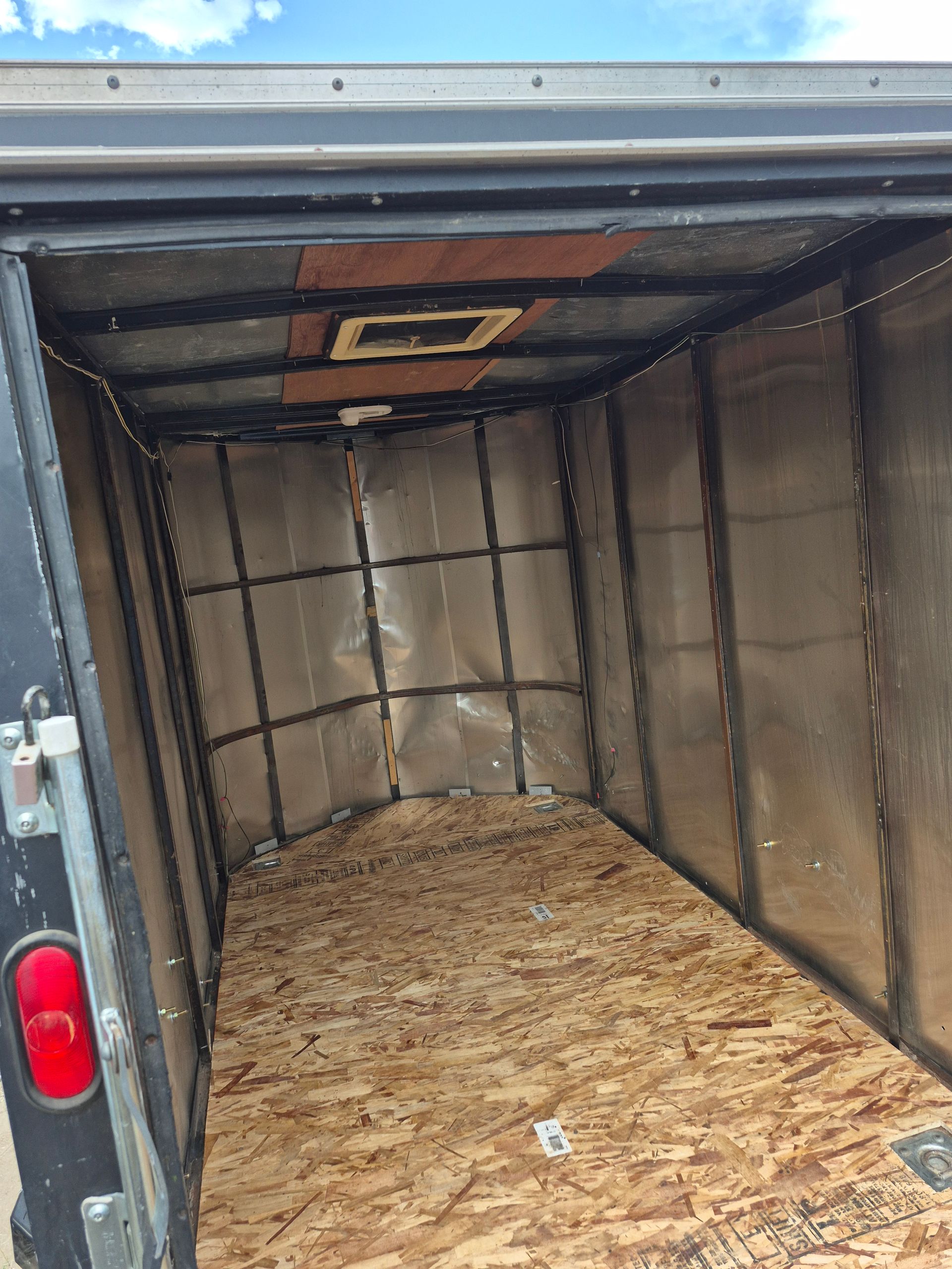 Interior of a cargo trailer. The walls are metal-clad with wood studs. The floor is plywood. A vent is in the ceiling.