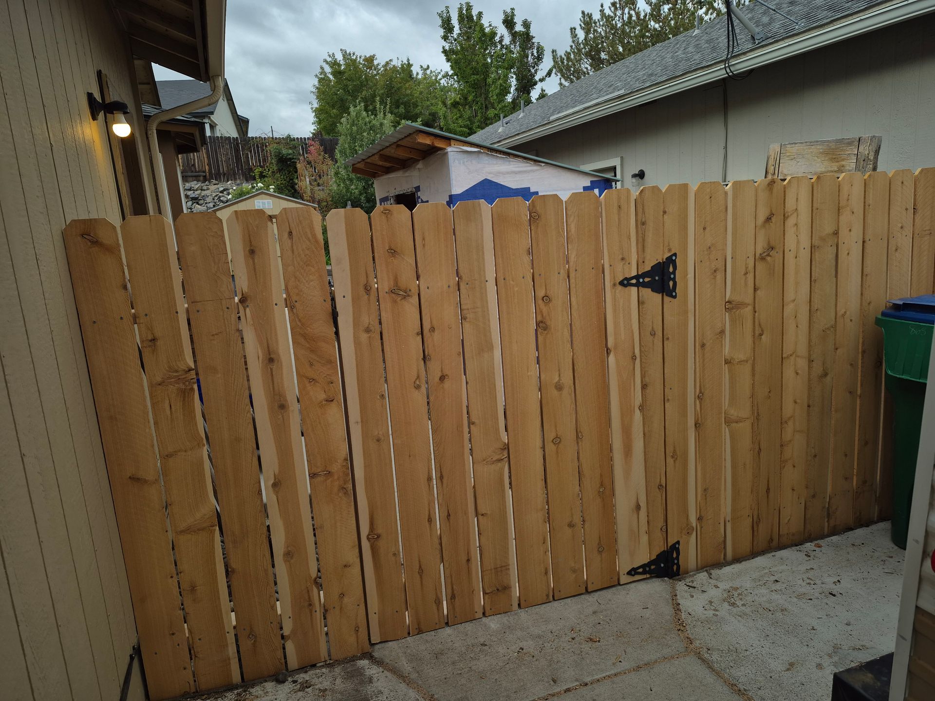 Wooden fence with gate, set against a concrete surface. Beige siding to the left.
