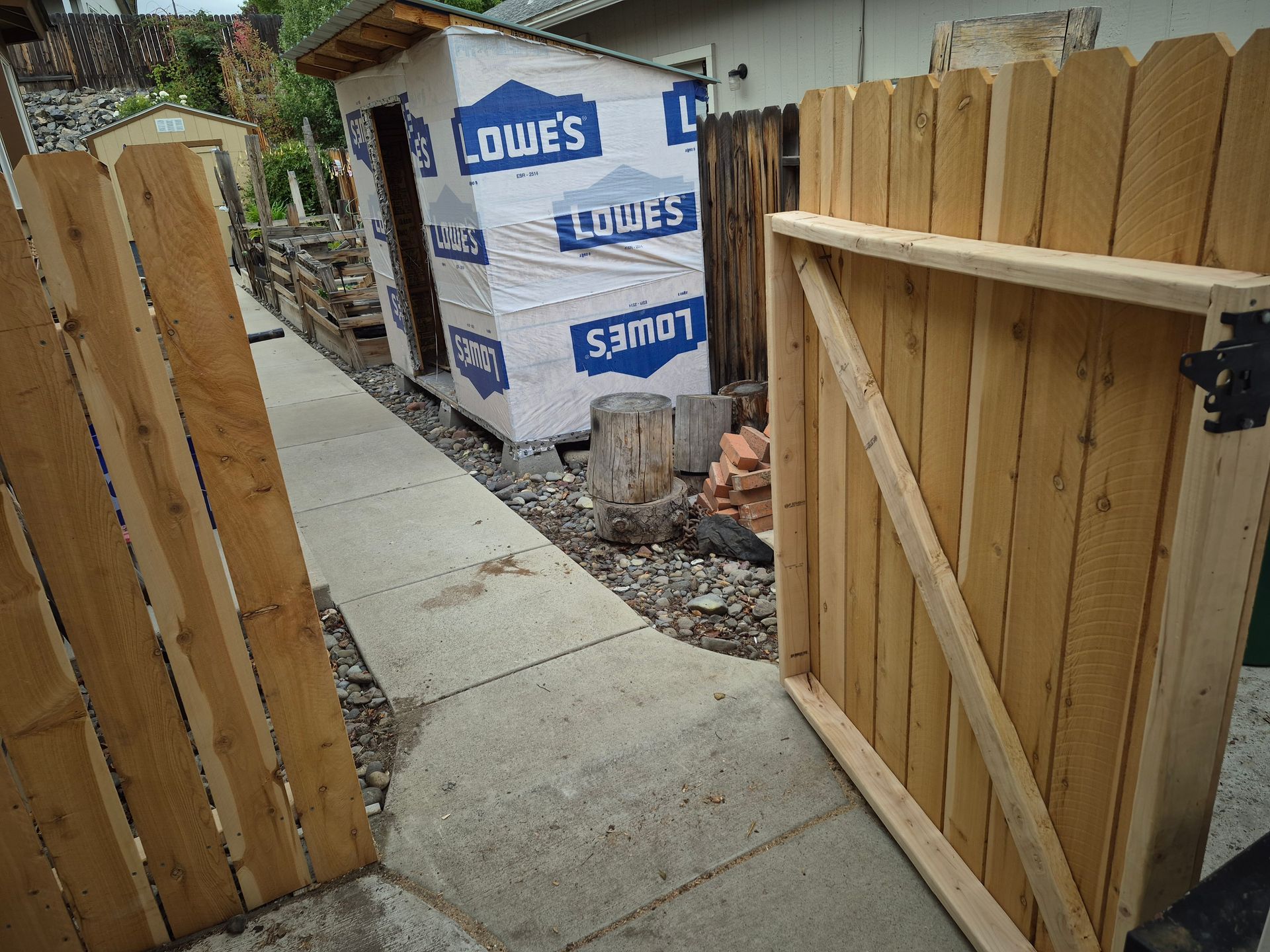 A wooden fence with a gate, a shed under construction, and a concrete path.