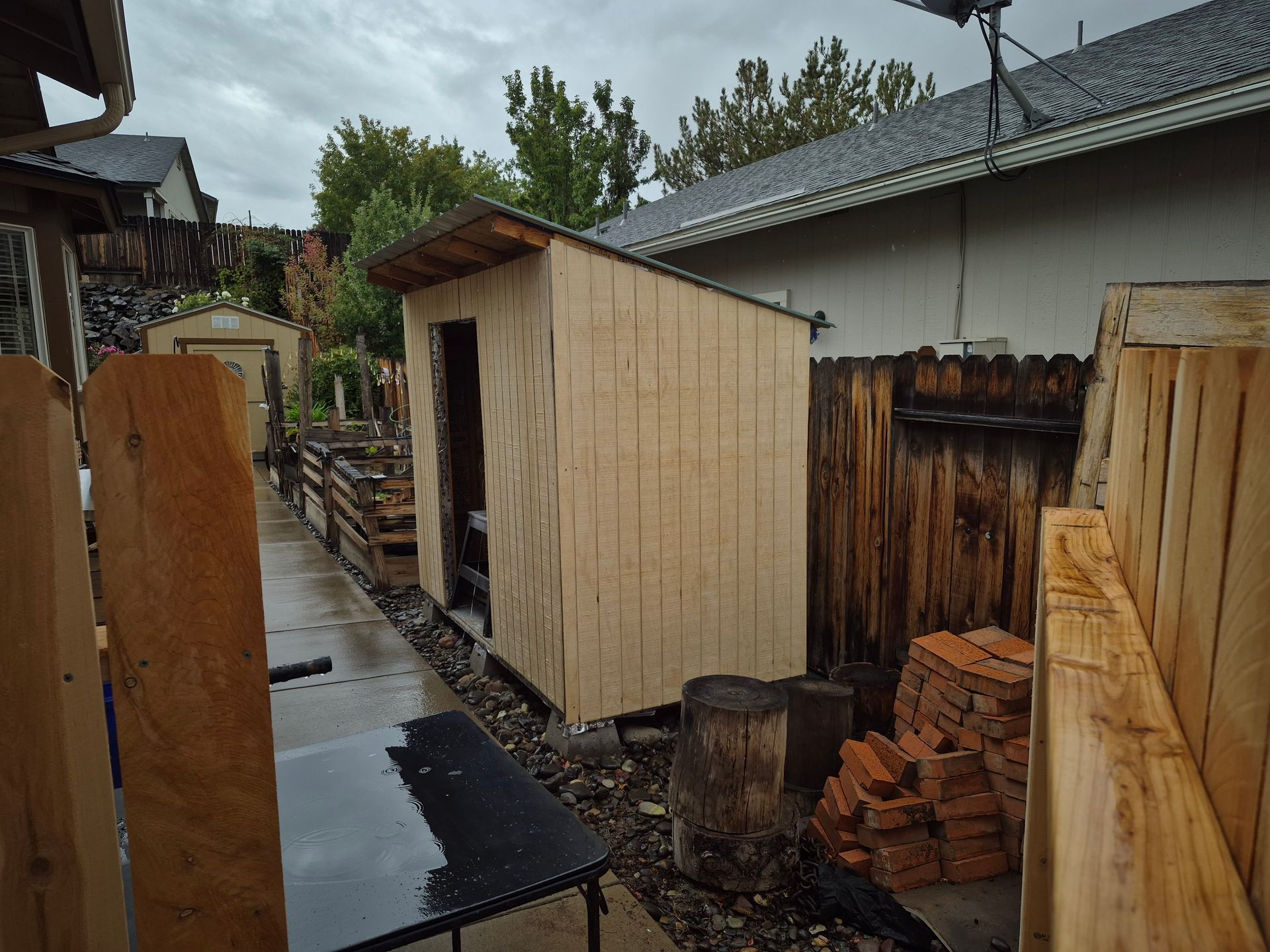 Shed next to a fence in a backyard. Raw wood on the shed and fence. Overcast day.