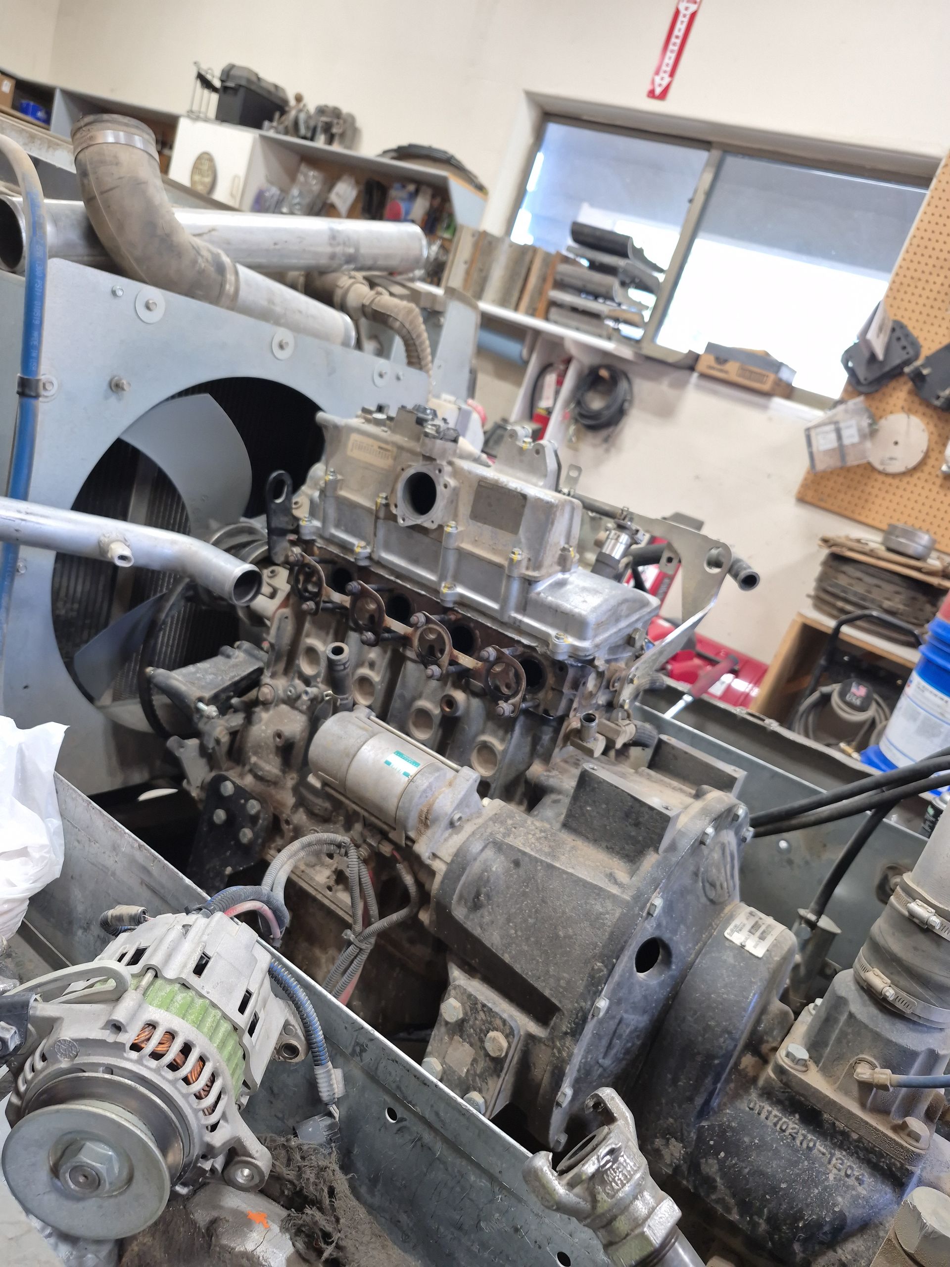An engine being worked on in a workshop; the engine is gray, with tubes and other equipment attached.
