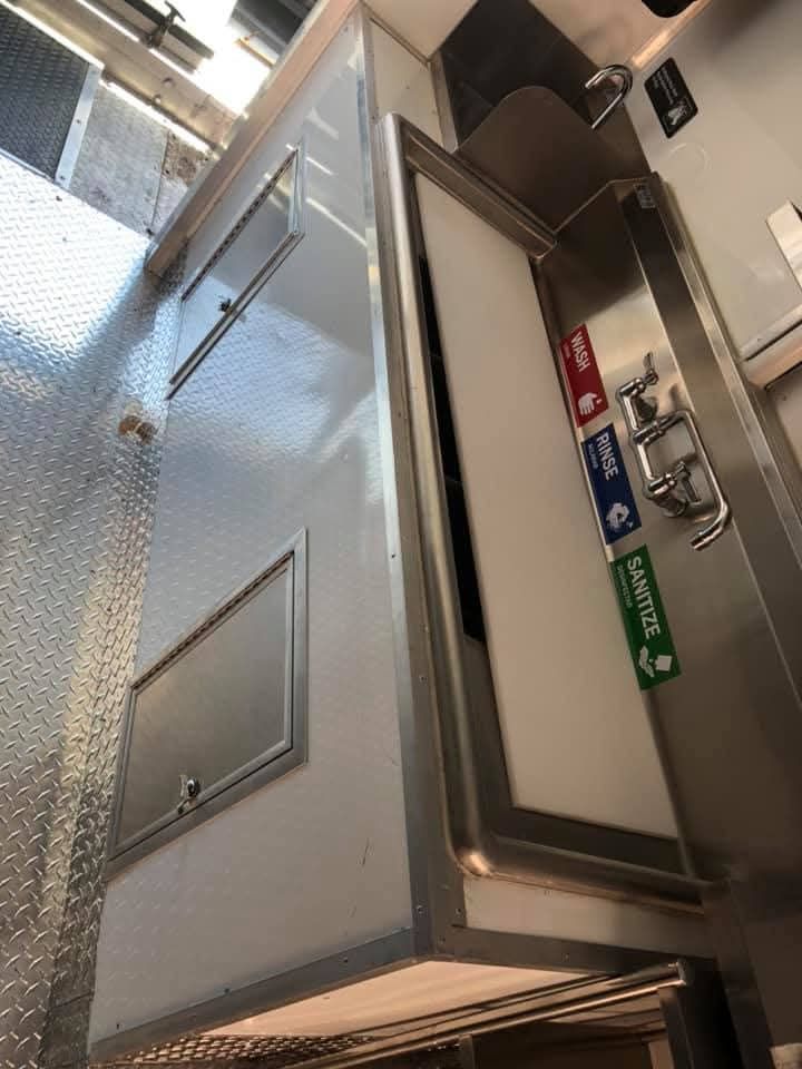Interior of a metal ambulance with cabinet, sink, and labeled trash receptacles.