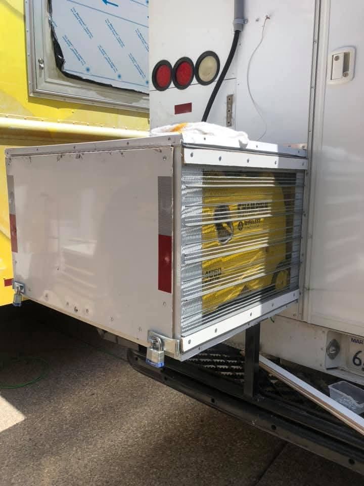 White metal box secured to the back of a truck, containing yellow bags visible through wire mesh.