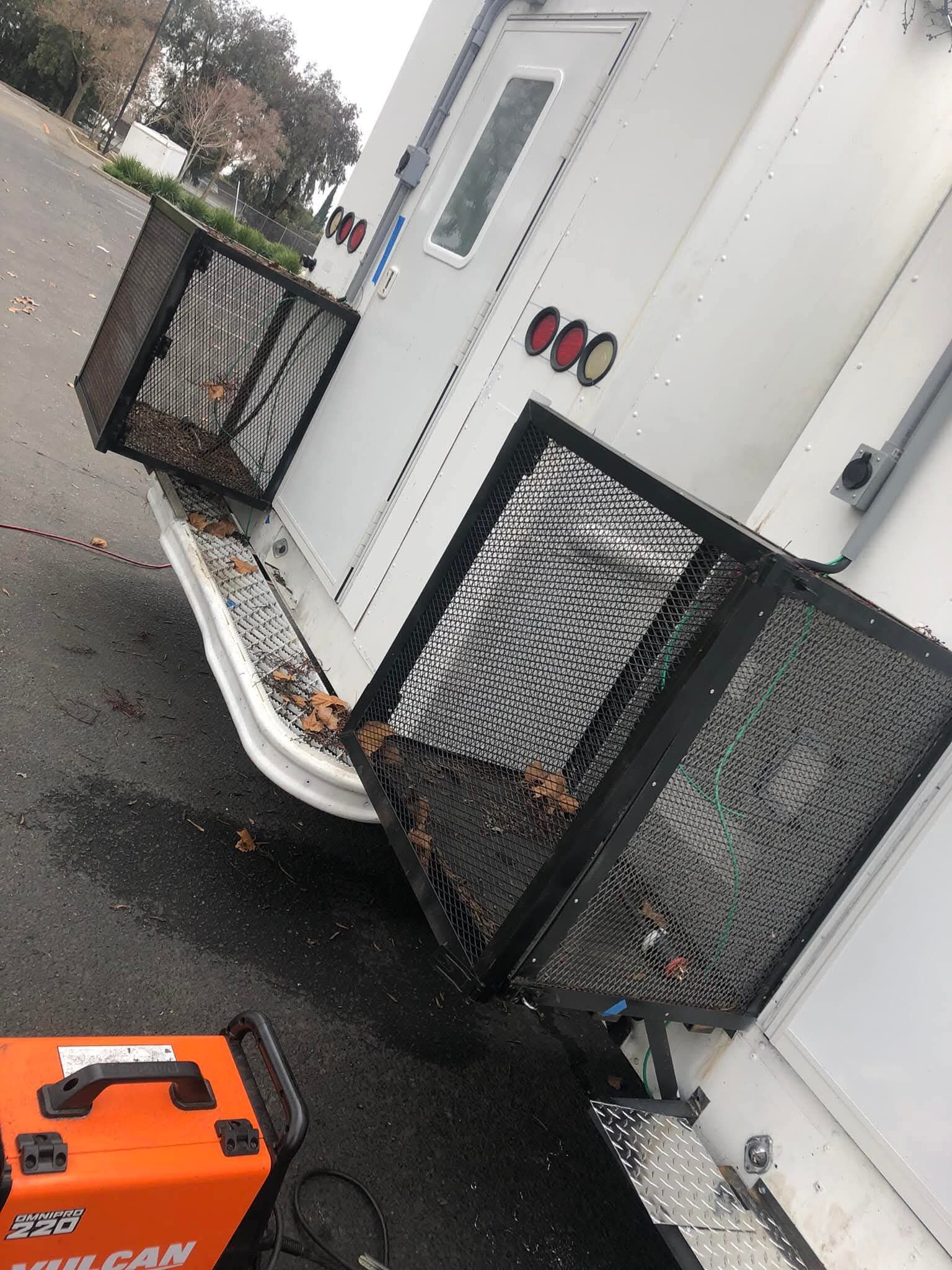 Rear of a white truck with two black metal baskets. An orange welder sits nearby.