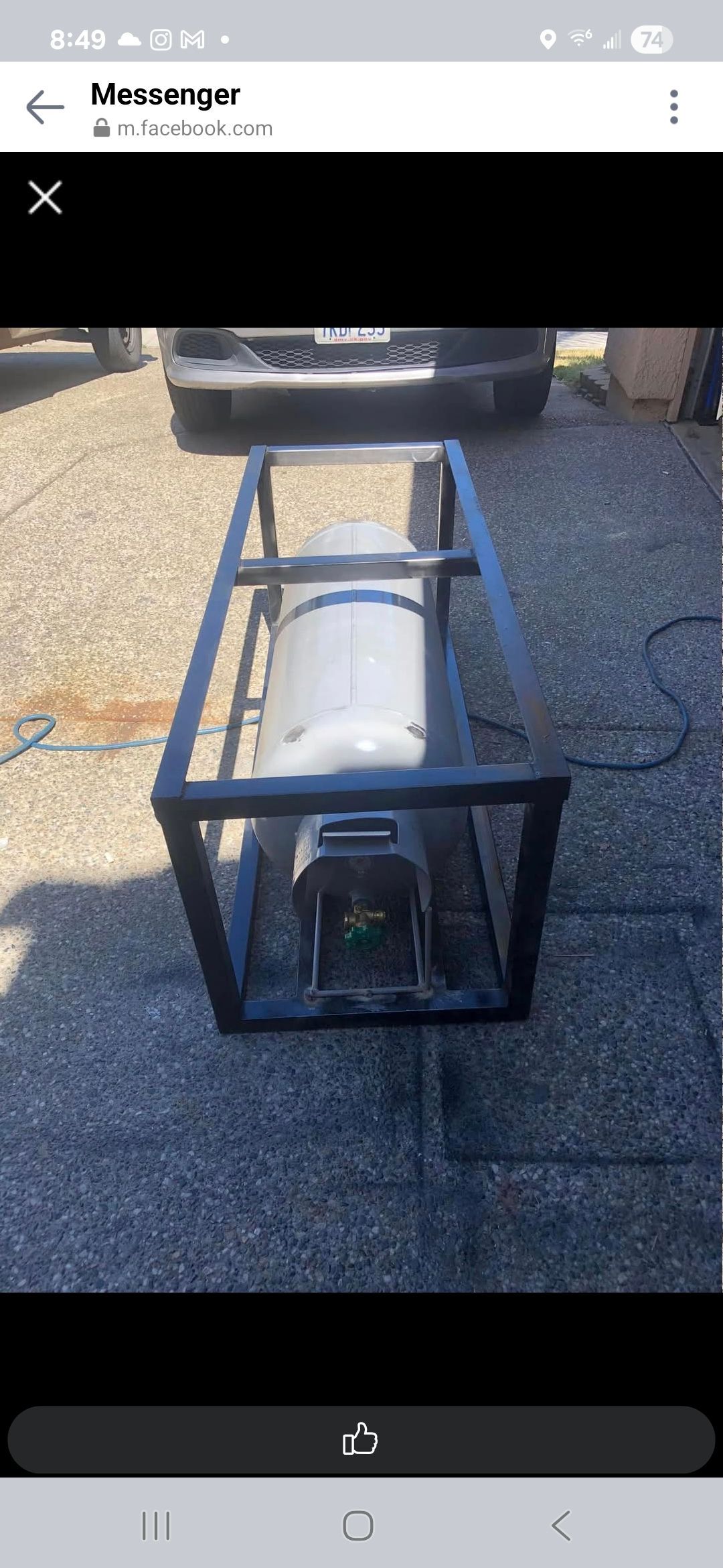 A metal cage contains a white tank-like object, likely a generator, on an asphalt surface. A vehicle is in the background.
