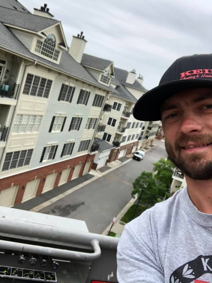 Man in a cap smiles, overlooking apartment buildings and a street on a cloudy day.