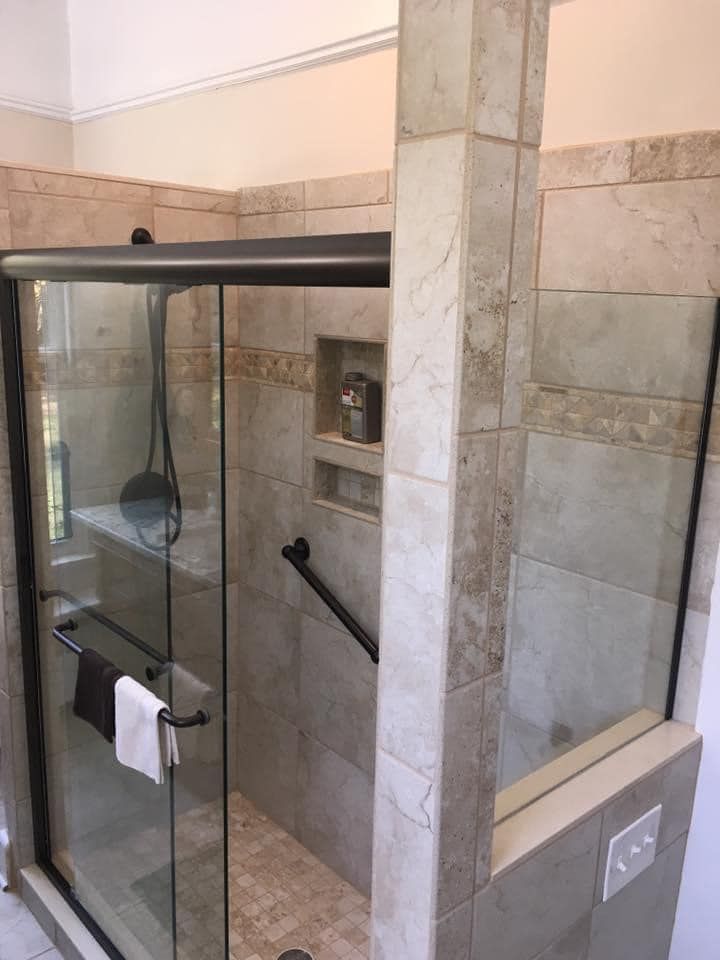 Shower with glass doors, tiled walls, grab bars, and a built-in shelf.