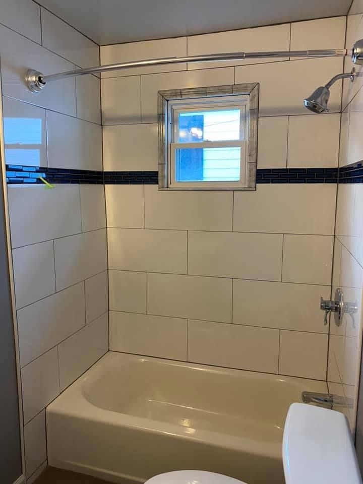 Bathroom with white tiled walls, a bathtub, and a small window. Blue and black accent tiles and chrome shower fixtures.