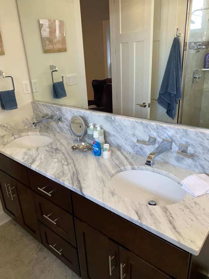 Bathroom with dark brown cabinets, marble countertop, and two sinks. A large mirror reflects the room.
