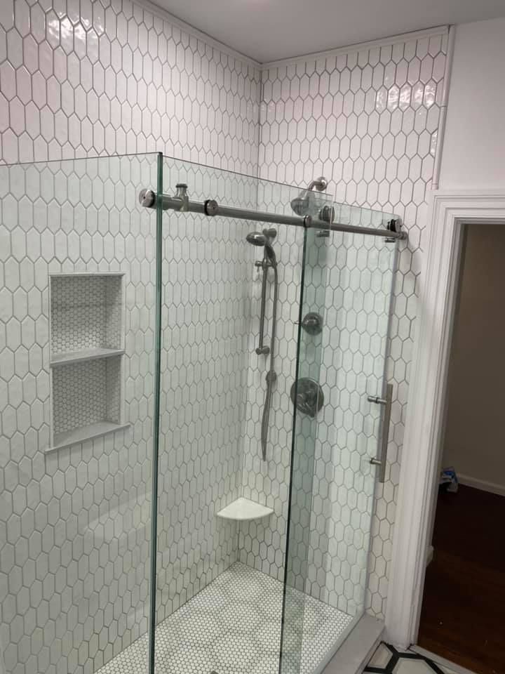 Tiled shower with glass sliding doors, silver fixtures, and a built-in shelf. White tiles in an oval pattern.