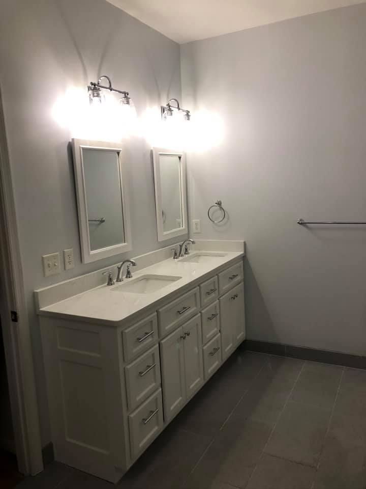 Bathroom with white vanity, two sinks, mirrors, and gray flooring; light blue walls.