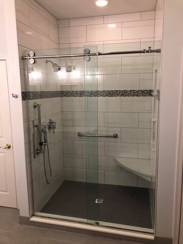Accessible shower with a sliding glass door, white and gray tiles, and grab bars.