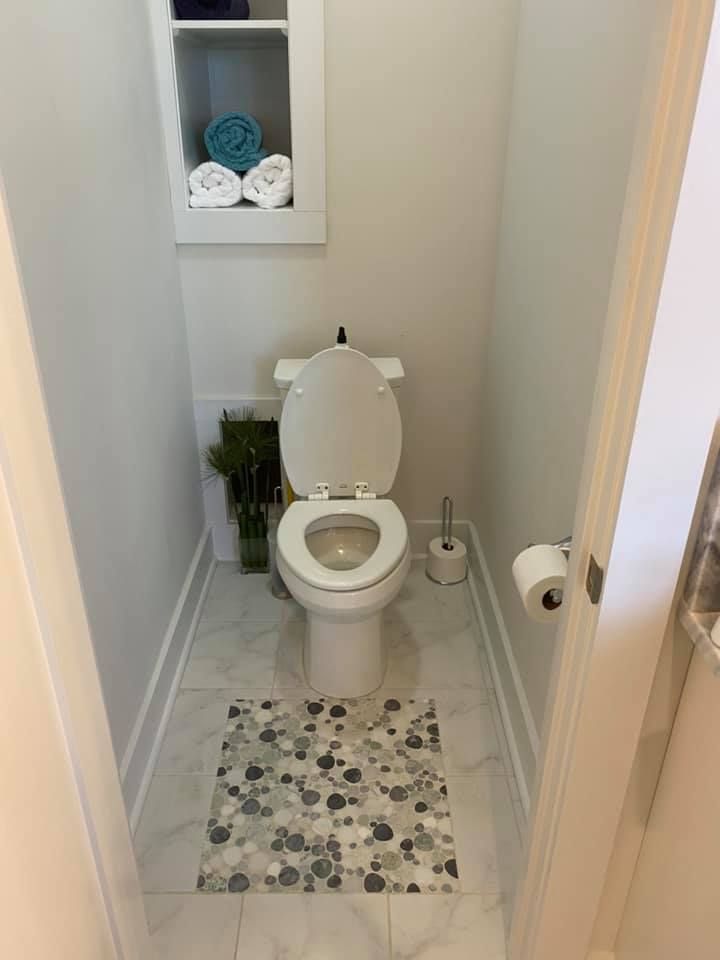 Small, modern bathroom with a toilet, decorative floor tile, and a built-in shelf holding towels.
