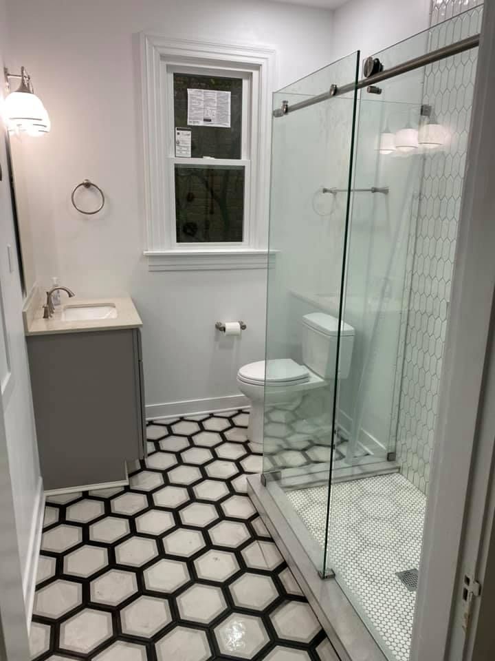 Bathroom with black and white hexagon floor tiles, glass shower, and gray vanity.