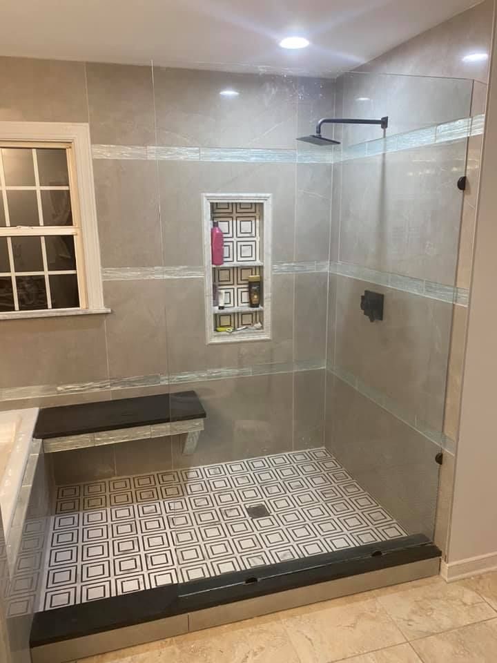 Modern shower with glass enclosure, gray and patterned tile, built-in bench, and recessed niche.