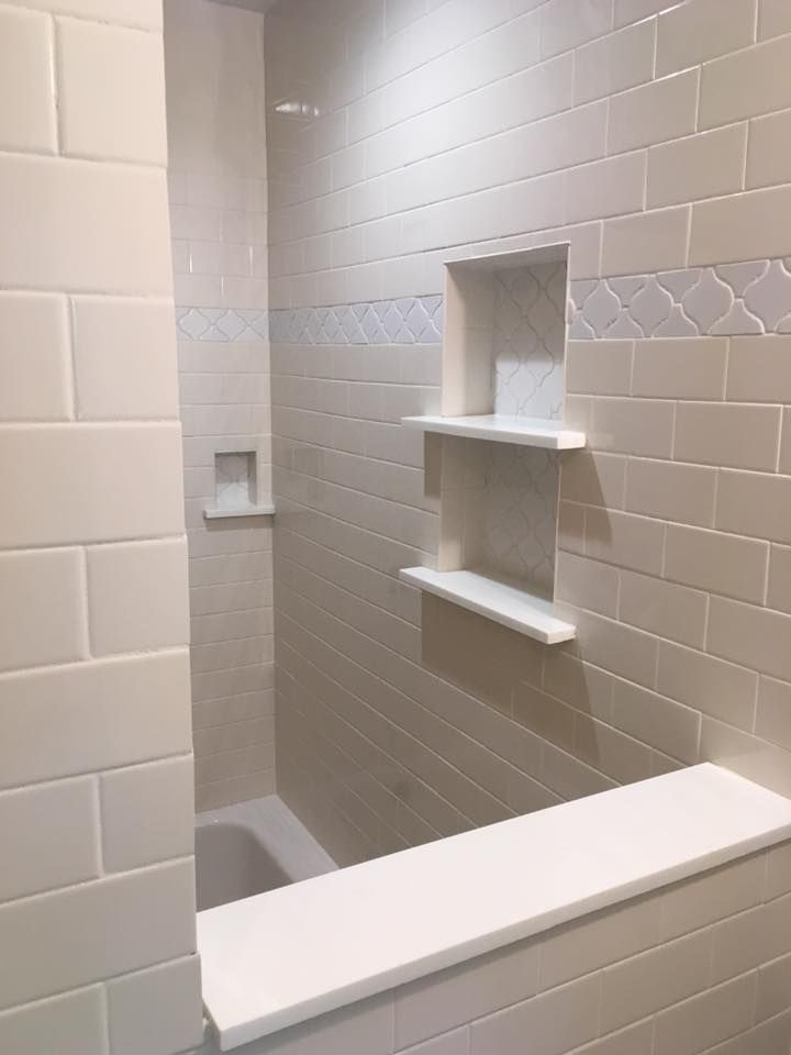 White tiled bathroom with built-in shelves, a tub ledge, and a small niche.