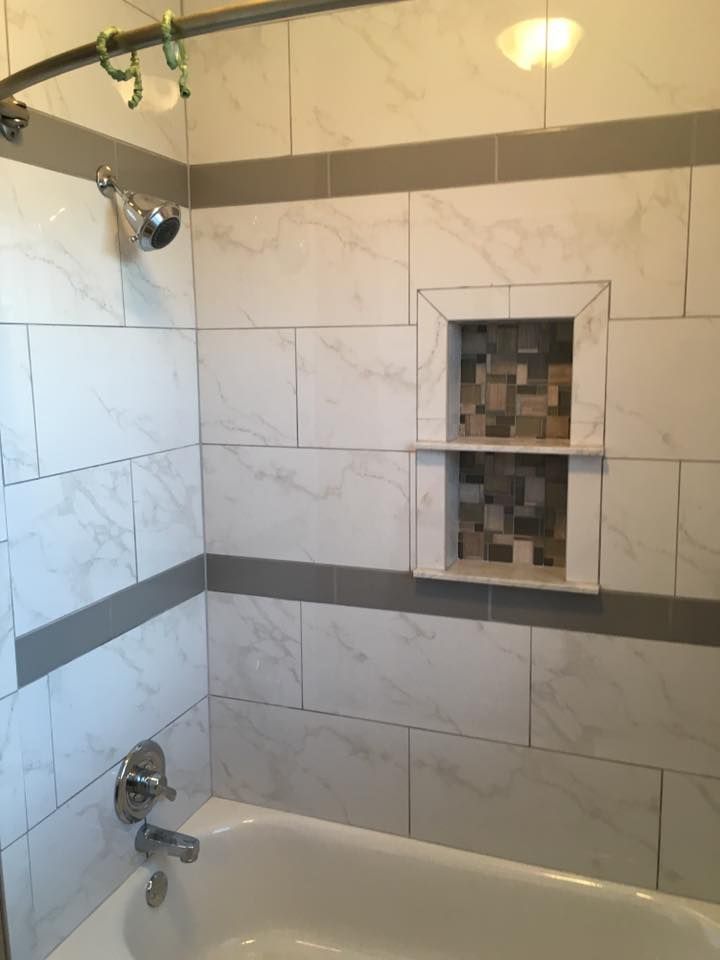 White tiled shower with gray trim, built-in shelf with mosaic tiles, chrome fixtures, and bathtub.