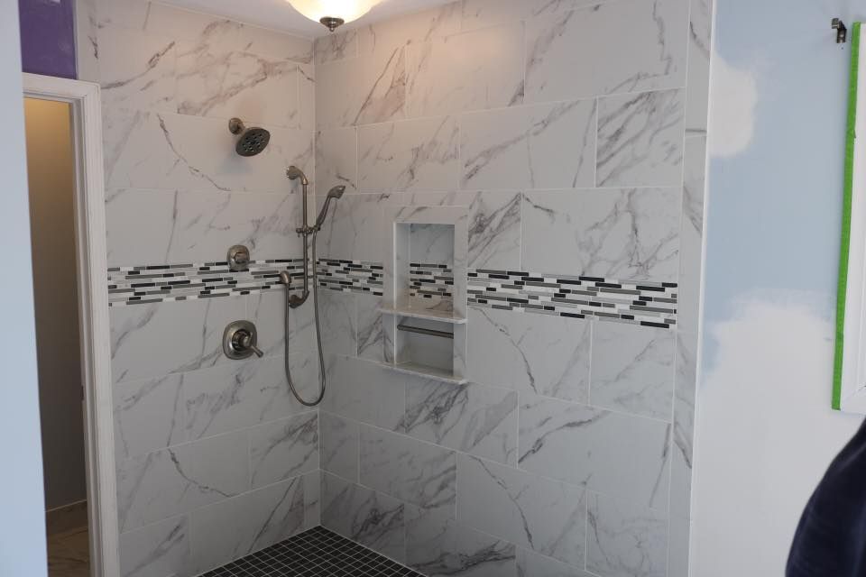 Marble-tiled shower with dark mosaic band and built-in shelf. Chrome shower fixtures.
