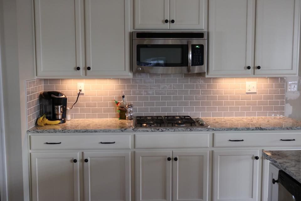 Kitchen with white cabinets, gray subway tile backsplash, stainless steel microwave, and granite countertops.