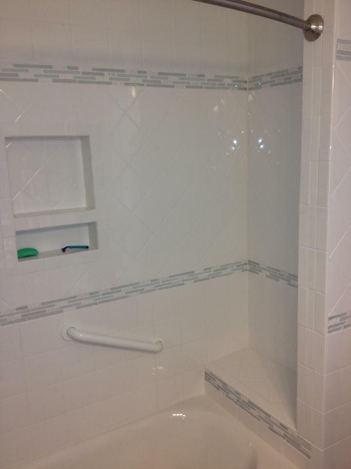 White tiled shower with a built-in niche, grab bar, and decorative blue tile trim.