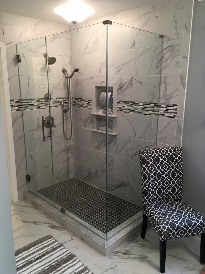 Modern bathroom with a glass-enclosed shower featuring marble tile, a patterned accent, and a decorative chair.